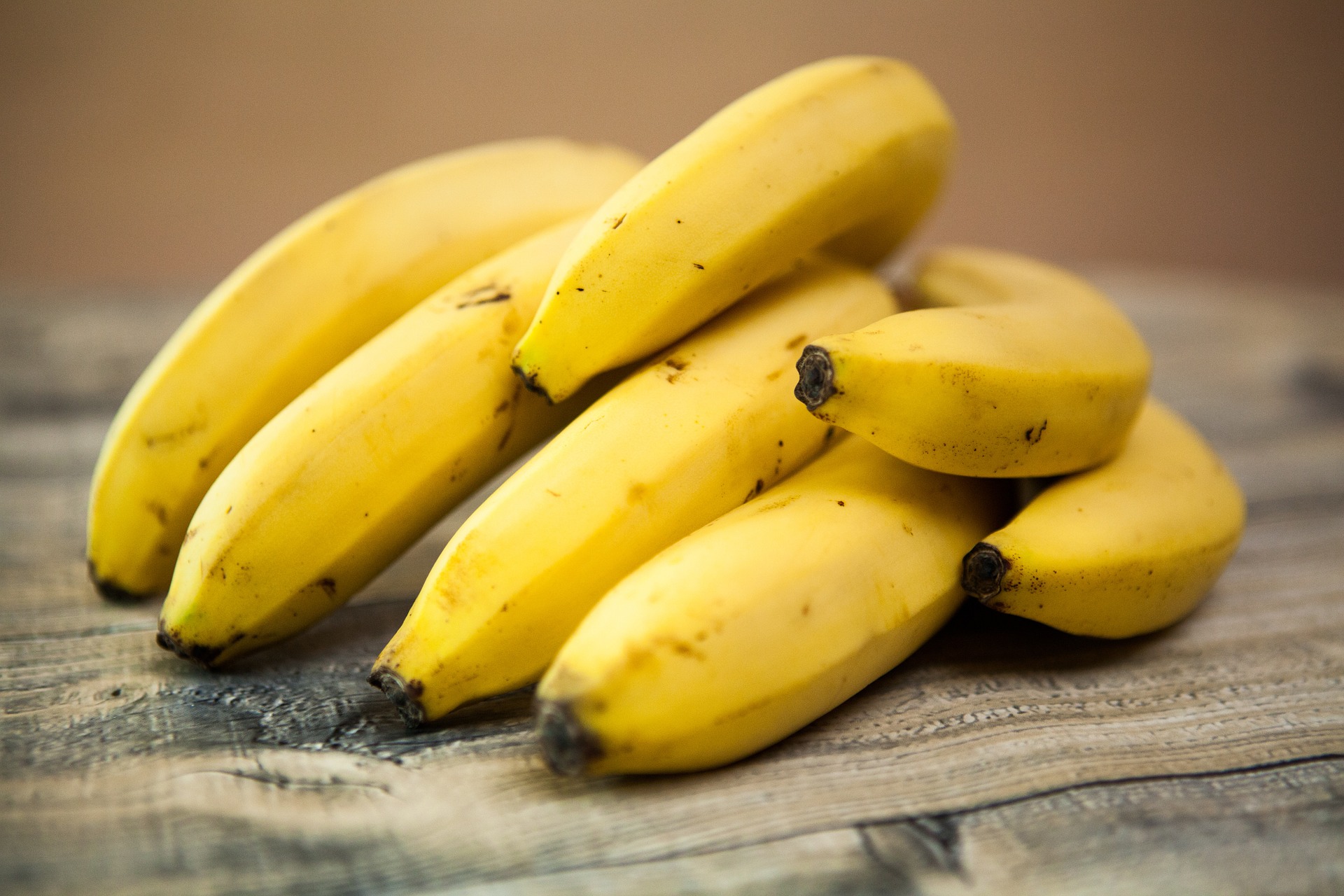 The basis of an easy diet - A Bunch of Seven Yellow Bananas laying on a cloth with a realistic wooden texture.